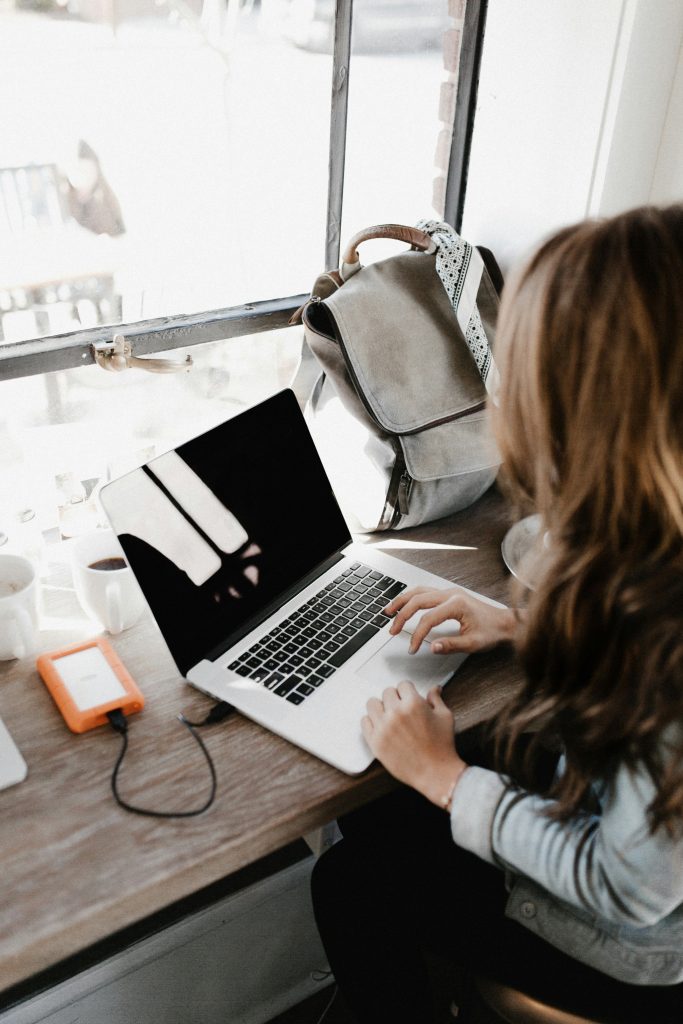 Person using a laptop at a wooden table, with a backpack and coffee cups nearby, illustrating e-commerce optimization and user experience in a cozy workspace.