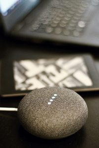 Smart speaker on a table with laptop in background, illustrating voice search optimization in digital marketing strategies.