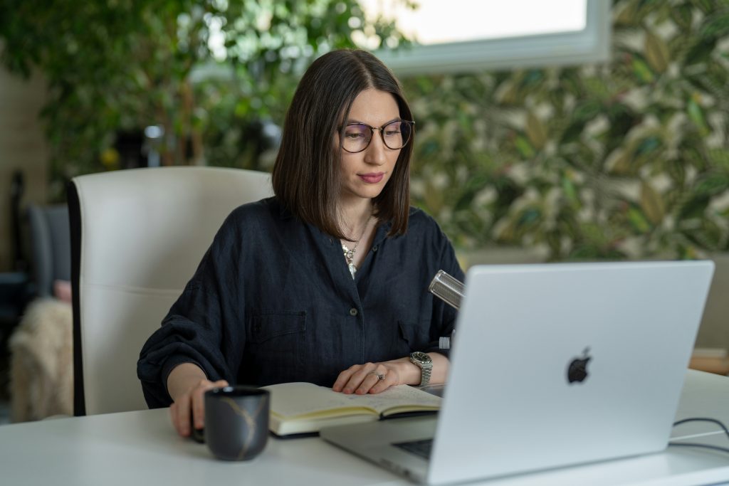 Woman working on a laptop in a modern workspace, with a coffee cup and notebook, reflecting themes of digital marketing and content curation.