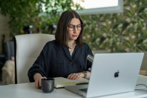 Woman with glasses working on a laptop in a modern office, emphasizing digital marketing and content creation.